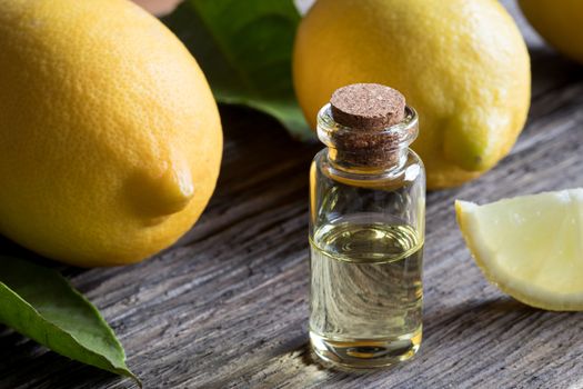 A bottle of lemon essential oil on old wood, with lemons in the background