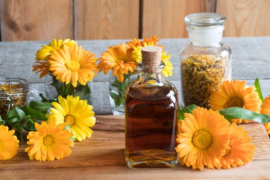 A bottle of calendula (marigold) tincture on a wooden table, with fresh and dry calendula flowers in the background