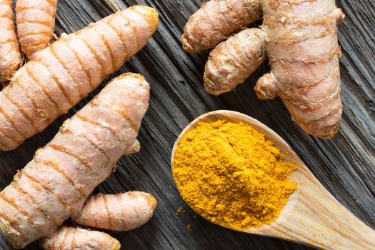 Turmeric powder and fresh turmeric root on a wooden background