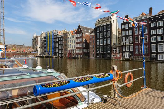 Spirngtime view of the Dancing Canal Houses of Damrak street, iconic canal houses in Amsterdam, Netherlands. Some sightseeing motorboats next to pier.