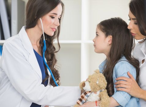 Pediatrician checks heart beat of a little girl in the arms of mother