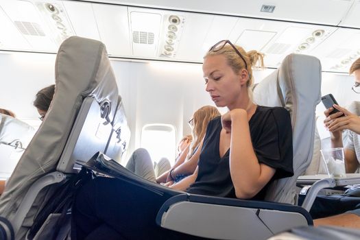 Female traveler reading magazine on airplane during flight. Female traveler reading seated in passanger cabin.