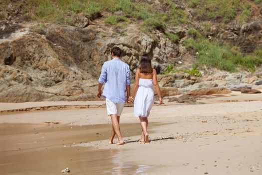 Happy couple walking on sand of tropical beach