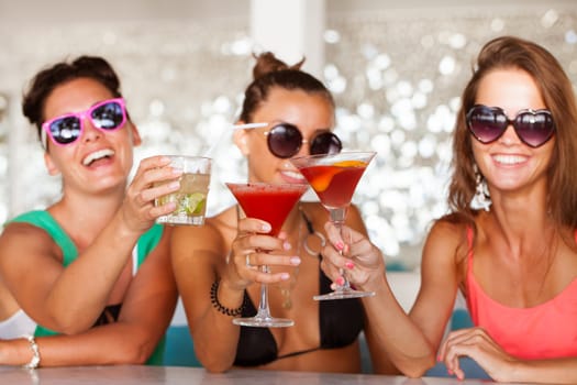 Three female friends sitting in summer cafe drinking cocktails