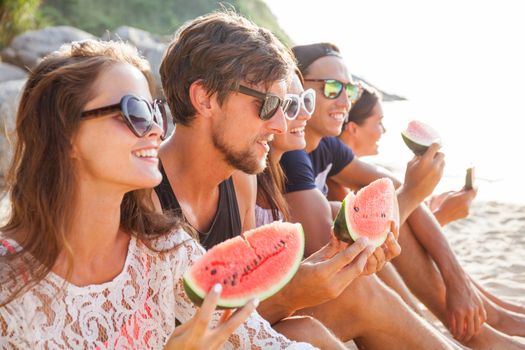 Happy young friends eating watermelon on beach