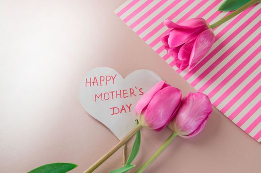 Flat lay composition with flowers and heart for mother's Day, greeting for women. Red tulips on pink background.