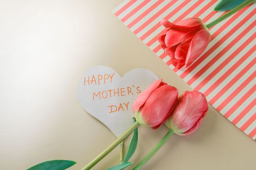 Flat lay composition with flowers and heart for mother's Day, greeting for women. Red tulips on pink background.