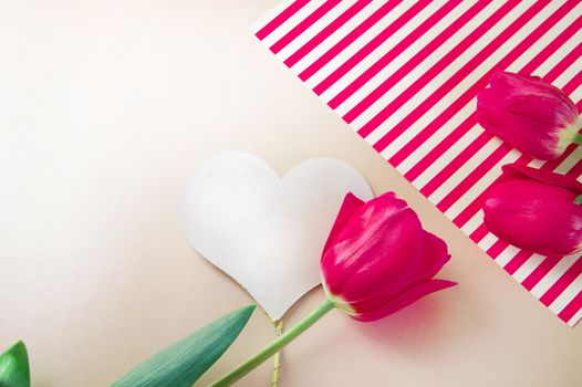 Flat lay composition with flowers and heart for mother's Day, greeting for women. Red tulips on pink background.