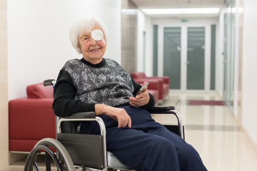 Elderly 95 years old woman sitting at the wheelchair using modern mobile phone application to monitor her therapy and entertain herself.