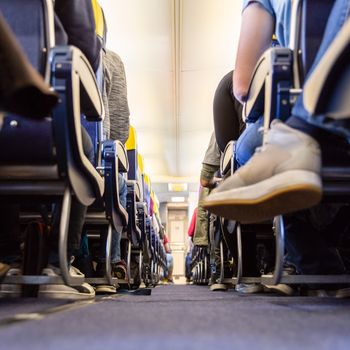 Low agle view of passenegers commercial airplane aisle with passenegers sitting on their seats while flying.