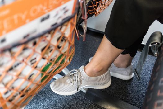 Female passenger with lack of leg space on long commercial airplane flight. Focus on casual sporty sneakers.