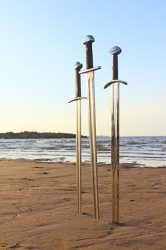 Three swords in sand of battlefield on sea beach