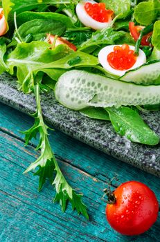 Vegetable salad with greens, cucumber, egg and red caviar.Green salad on rustic background