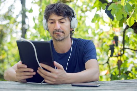 young man holding a tablet with headphones, outdoor