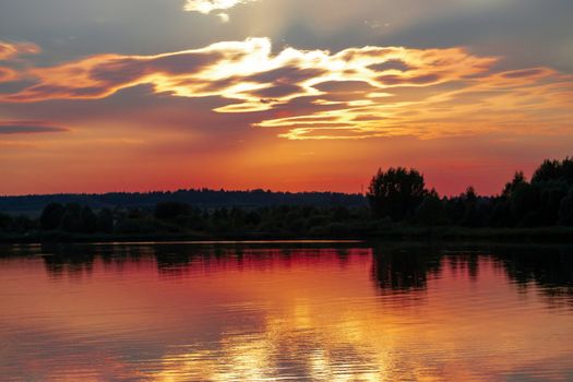 Panorama reflection of sunset in the water of the lake. The sky and clouds, illuminated by the sun setting over the horizon, acquired unusual red, orange and gray colors.