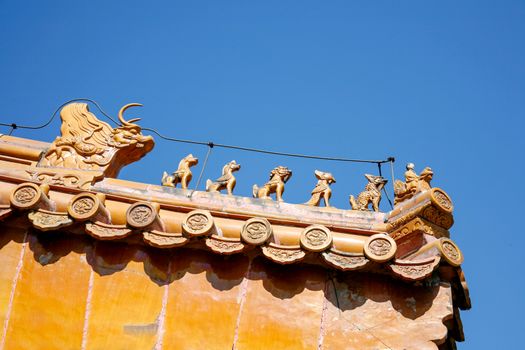 Roof of traditional chinese temple with orange ceramic tiles and an ornate red stone gable