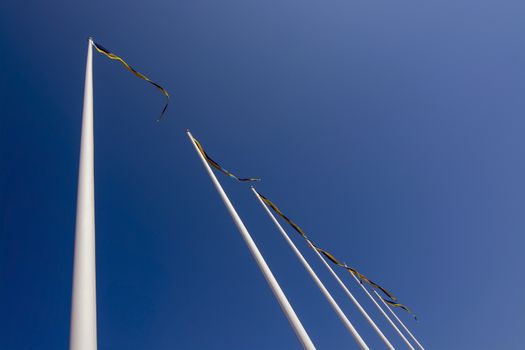 Swedish flagpoles in a diagonal row with blue and yellow pennants on a sunny day against blue sky.