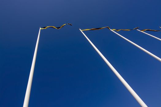 Swedish flagpoles in a row with blue and yellow pennants on a sunny day against blue sky.