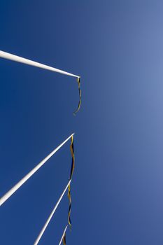 Swedish flagpoles in a vertical row with blue and yellow pennants on a sunny day against blue sky.