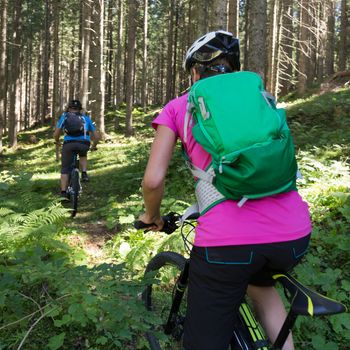 Active sporty couple riding mountain bikes on demanding forest trail.