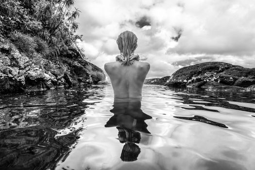 Rear view of beautiful naked woman bathing and relaxing in natural swimming pool before the 500 feet waterfall in natural park on tropical island of Mauritius. Black and white image