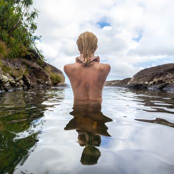 Rear view of beautiful naked woman bathing and relaxing in natural swimming pool before the 500 feet waterfall in natural park on tropical island of Mauritius.