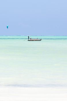 Solitary fishing boat and a kite surfer on picture perfect white sandy beach with turquoise blue sea, Paje, Zanzibar, Tanzania. Copy space.