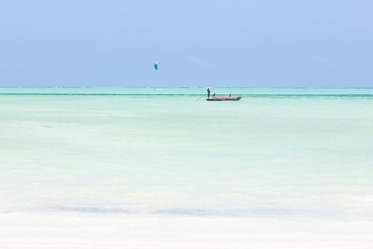 Solitary fishing boat and a kite surfer on picture perfect white sandy beach with turquoise blue sea, Paje, Zanzibar, Tanzania. Copy space.