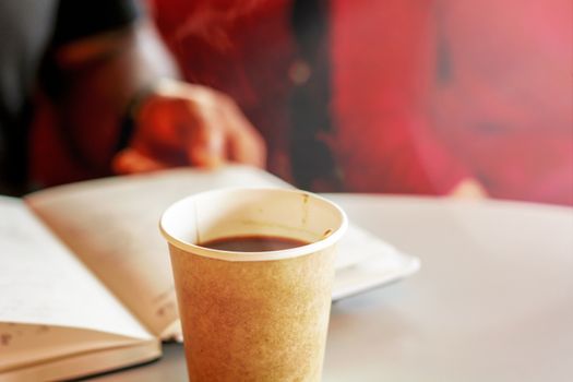 coffee in a recycled paper container with people reading and relaxing in the blurred background. Coffee break. Environmental Protection. Relaxing moment