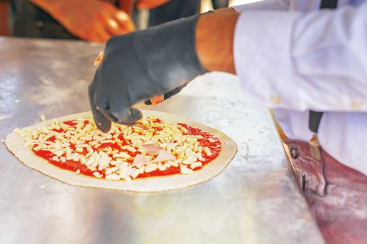 Pizza maker preparing a pizza by putting ingredients on top of the dough with tomato sauce and mozzarella. Italian cuisine. Famous recipe. Tasty food