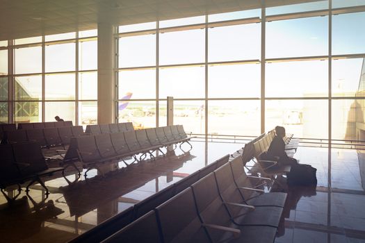 stained glass window of the departure hall inside an airport with a girl sitting on chairs waiting for her flight