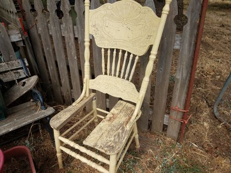 old broken wood chair with no seat bottom near wooden fence