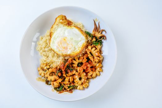 Spicy stir fried squid with basil leaves and chili, Sunny side up egg, served with brown rice. Hot and spicy dish.
