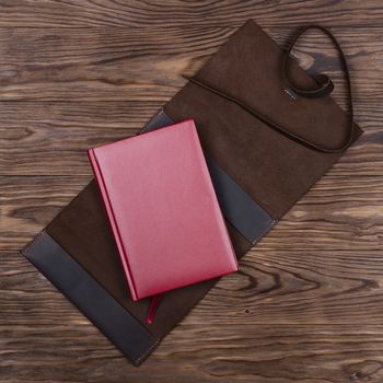 Brown opened handmade leather notebook cover with red notebook inside on wooden background. Stock photo of luxury business accessories.