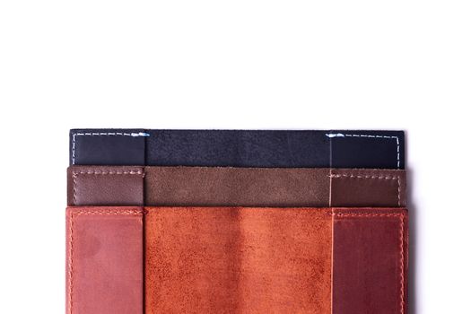 Three handmade leather passport covers stack isolated on white background. Closeup view. Covers are dark blue, red, brown and opened.