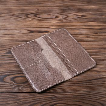 Light brown color handmade leather porte-monnaie on wooden textured background. Purse is opened and empty. Side view. Stock photo of luxury accessories.