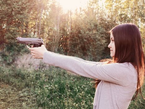 Pretty young Girl aiming from a pneumatic gun, outdoors.