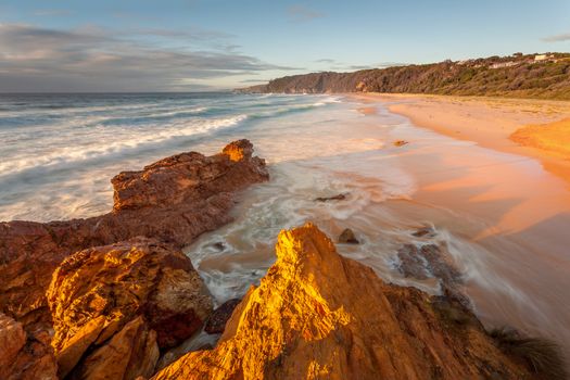 Early morning sunlight on the beach,soft foamy  waves wash onto the golden sands of the beach and swirl around exposed rocks