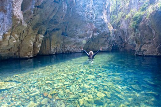 Sunlight streams into the Mares Forest Creek Canyon filled with the cilly blue water rich in minerals from the limestone rocks which give it its colour.  A woman makes the journey through the canyon