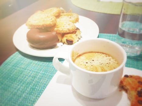 morning breakfast with a cup of frothy cappuccino with pastry and chocolate donuts. Sweet and unhealthy food. Table set with white ceramics