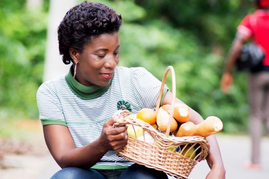 crouching young woman holds on his thigh a basket of food and look smiling.