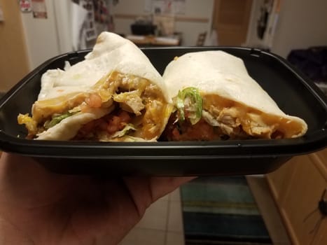 hand holding tortilla wrap with chicken and cheese in kitchen