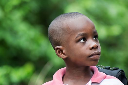 this child sitting next to a backpack looks aside on a green background.