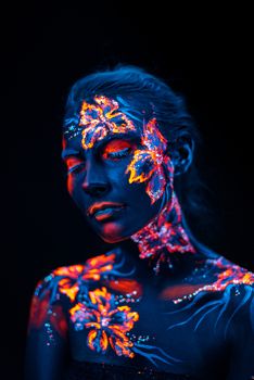 Conceptual face art with shining flowers painted in fluorescent colors isolated on black background