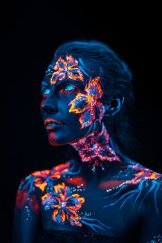 Conceptual face art with shining flowers painted in fluorescent colors isolated on black background