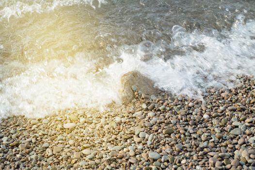 Sea wave on the shore of a pebble beach, water, foam, background.