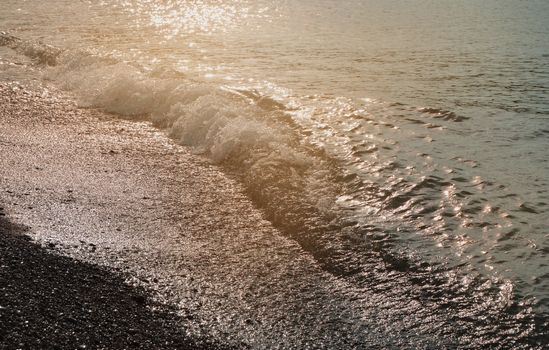 Shiny silver water on the sea pebble beach, early morning sunrise.