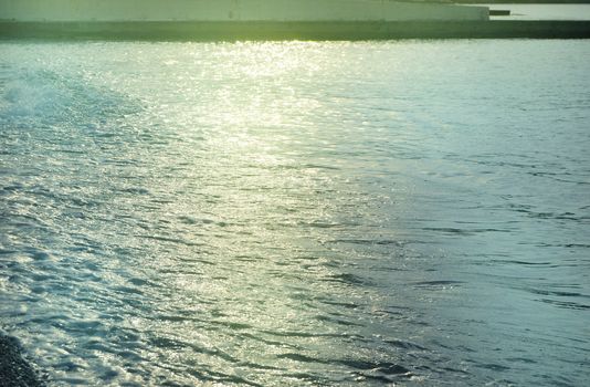 Shiny silver water on the sea pebble beach, early morning sunrise.