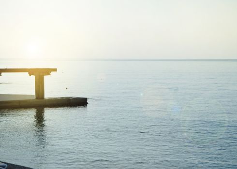 Sunrise on the sea with sun glare, pier on the shore in the early morning, calm, rest, summer holiday concept.