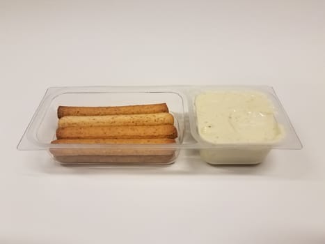 bread sticks and cheese spread in plastic container on white desk or surface